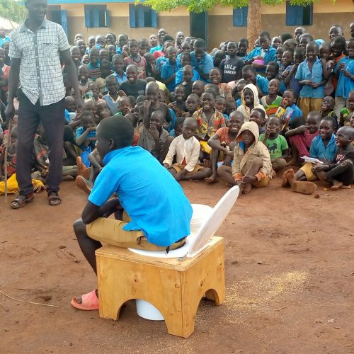 A student demonstrating how to sit on the compost toilet as opposed to squatting in Ayaka Primary School.